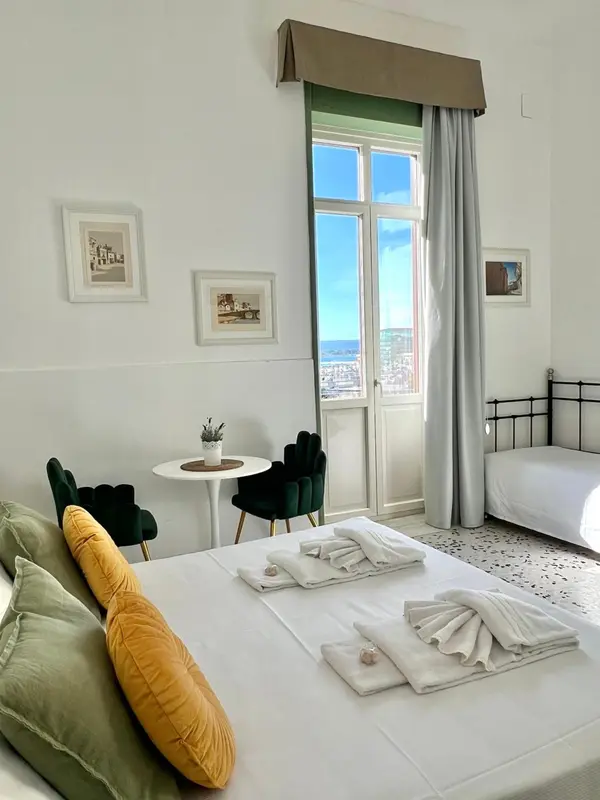 Une chambre lumineuse avec un lit fait et un coin salon près d'une fenêtre.