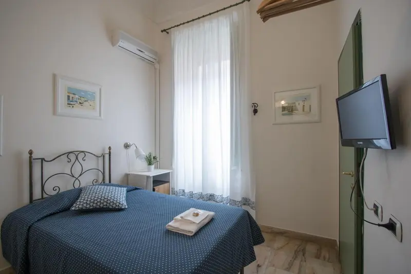 Une chambre lumineuse avec un lit simple et une télévision murale.