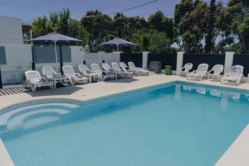 Transats blancs disposés autour d'une piscine ensoleillée.