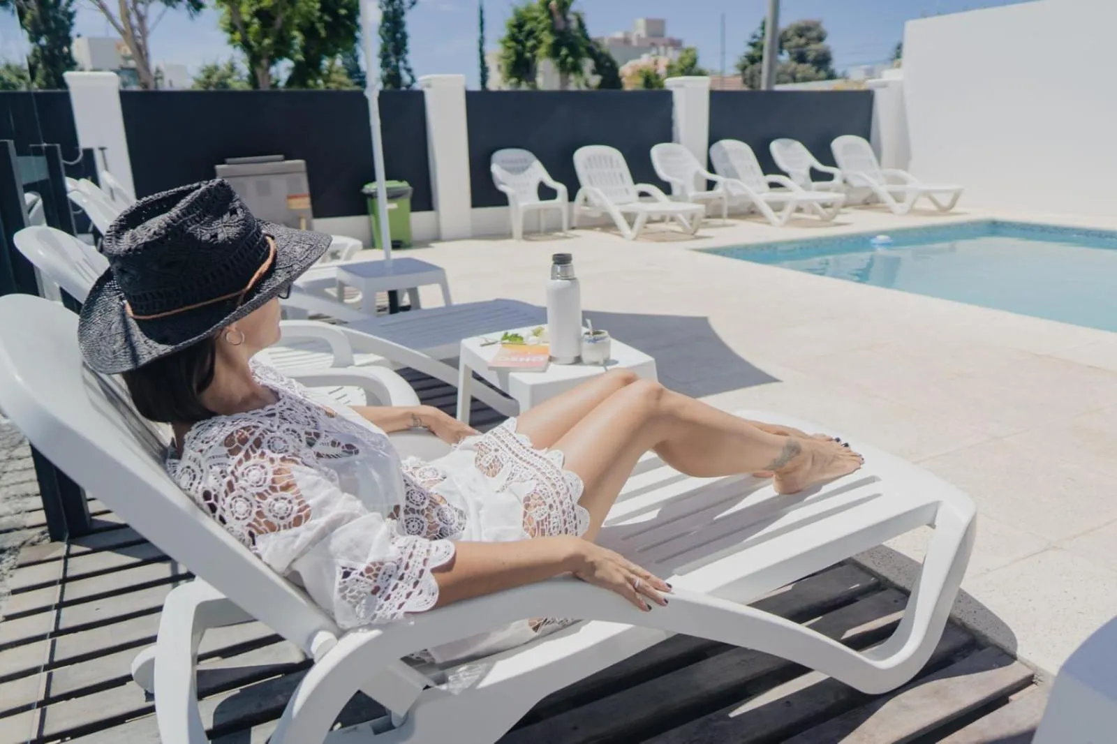 Une femme se relaxe au soleil sur une chaise longue près d'une piscine.