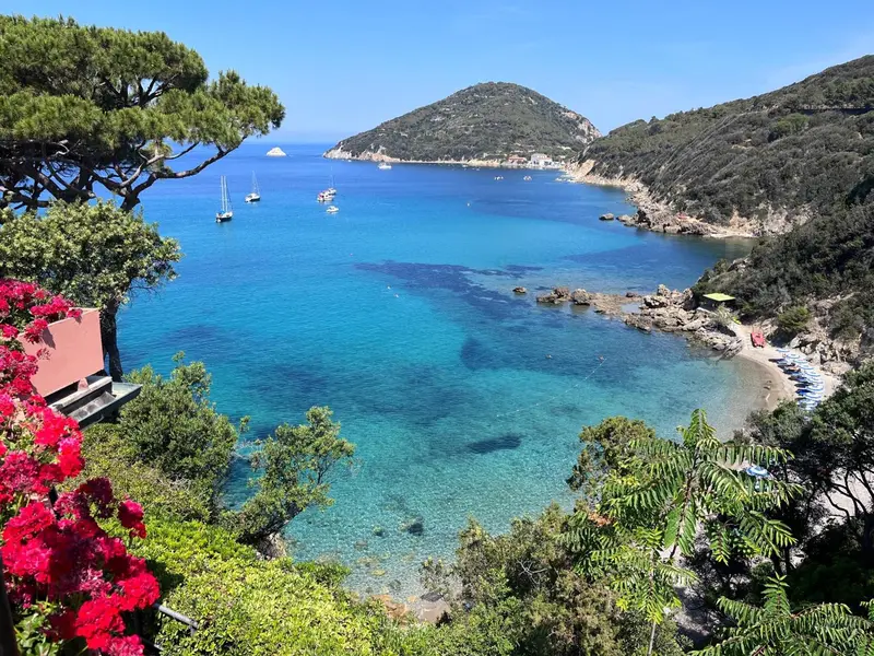 Vue aérienne d'une crique turquoise bordée de végétation et de quelques bateaux.