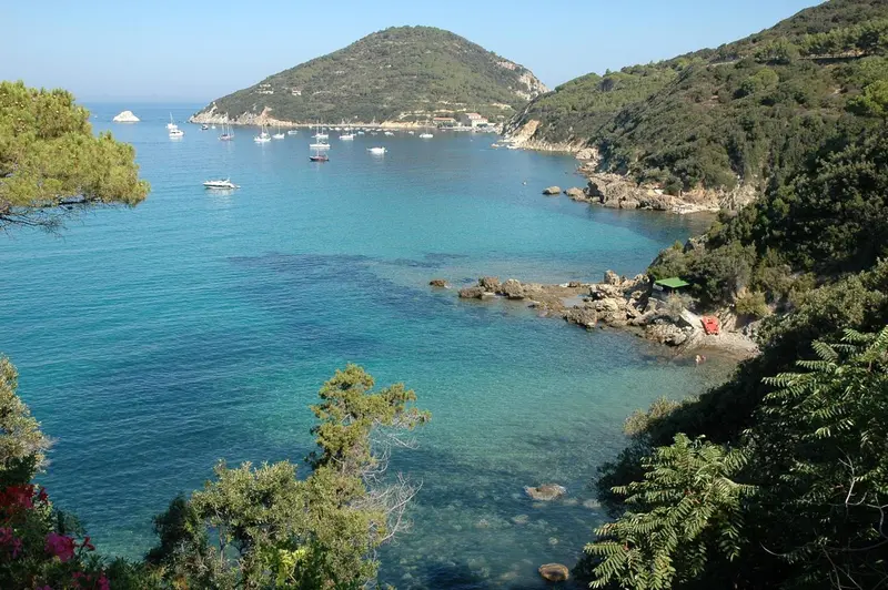 Une crique abritée avec des bateaux à voile amarrés dans une eau turquoise.