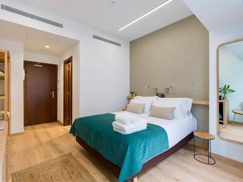 Une chambre lumineuse avec un grand lit recouvert d'une couverture turquoise.