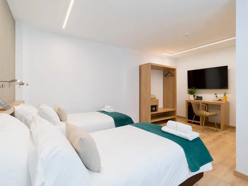 Chambre lumineuse avec deux lits simples et un espace bureau.
