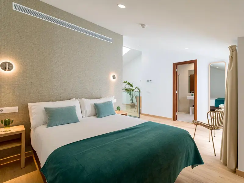 Une chambre lumineuse avec un grand lit recouvert d'une couverture turquoise et de coussins assortis.