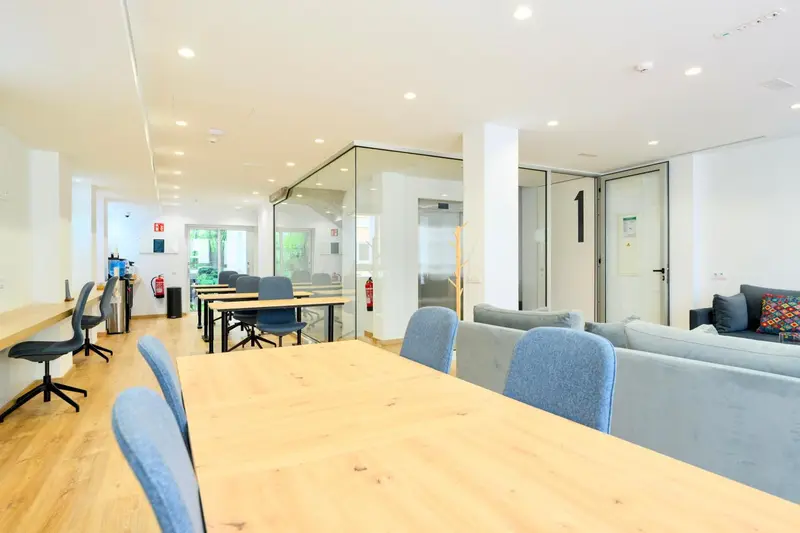 Une salle lumineuse avec des tables de travail et un coin salon.