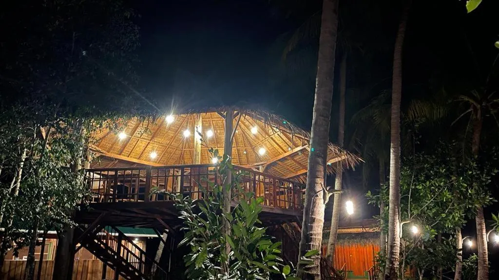 Un restaurant en plein air éclairé par des guirlandes lumineuses se dresse au milieu d'une végétation tropicale.