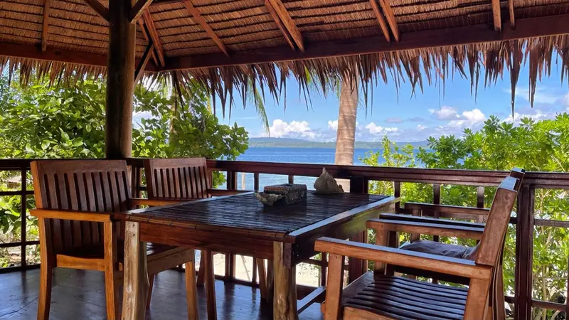 Une table et des chaises en bois sont disposées sur une terrasse couverte.