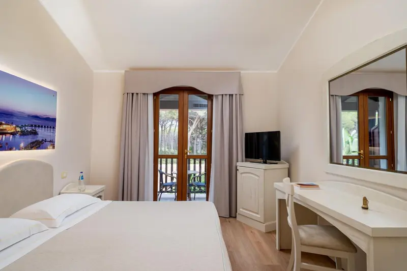 Chambre lumineuse avec un lit blanc et un accès à un balcon.