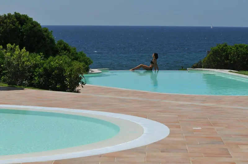 Une femme est assise au bord d'une piscine à débordement avec vue sur la mer.