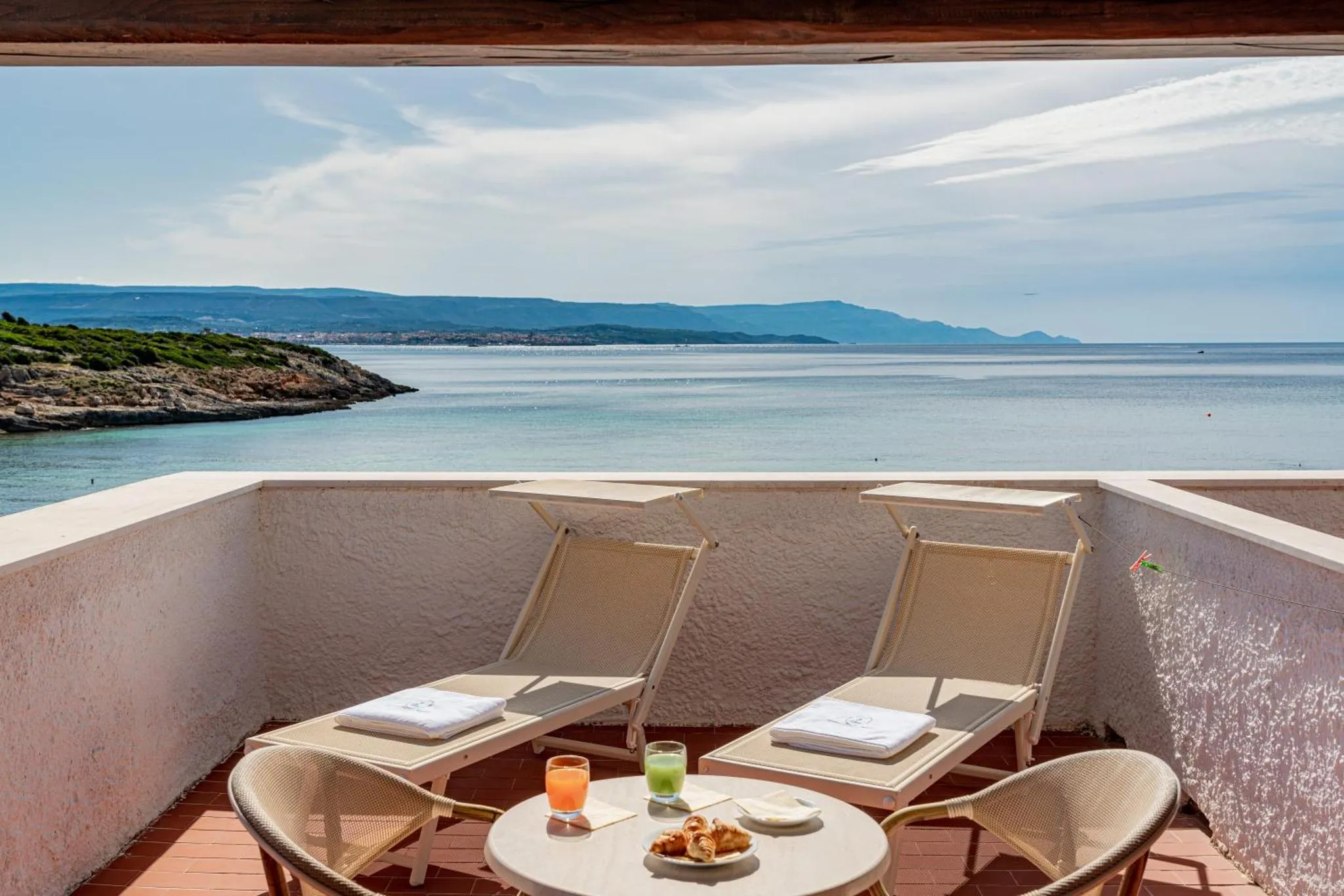 Deux transats et une table basse avec des boissons et des en-cas sur une terrasse avec vue sur la mer.