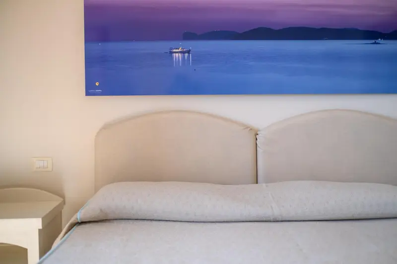 Un lit est devant un grand tableau représentant une scène marine au coucher du soleil.