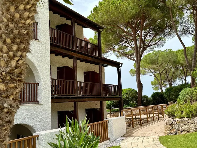 Bâtiment blanc à deux étages avec balcons en bois et végétation luxuriante.