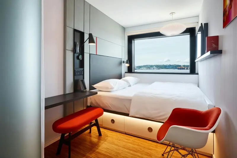 Une chambre moderne avec un lit blanc et des sièges colorés près d'une fenêtre.