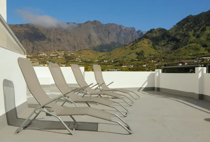 Transats alignés sur une terrasse avec vue sur des montagnes verdoyantes.