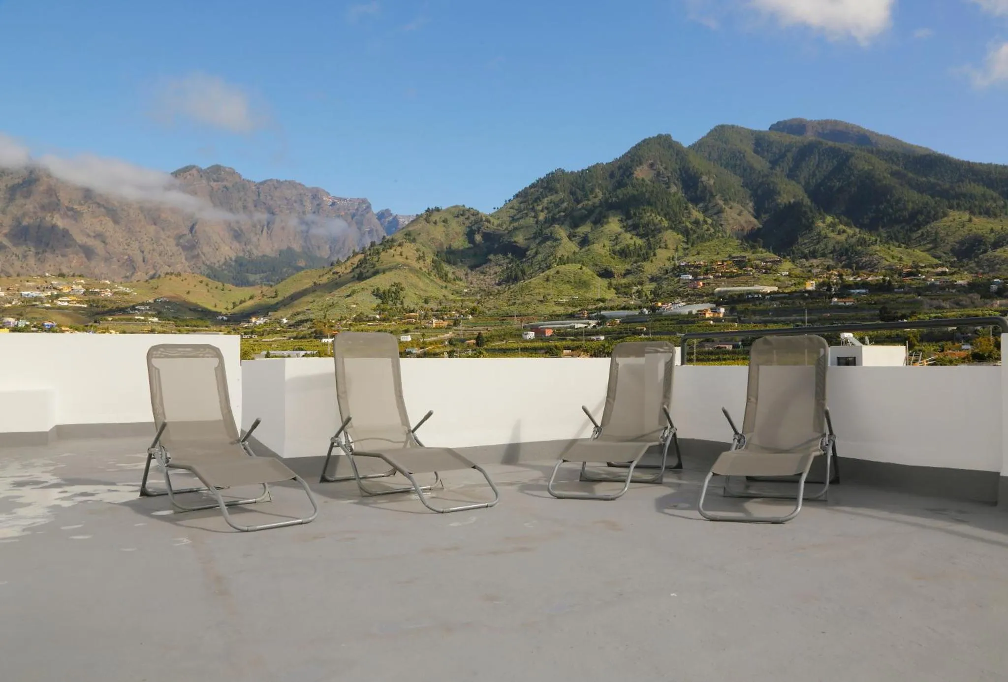 Transats alignés sur une terrasse offrant une vue sur des montagnes verdoyantes.