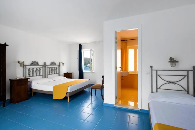 Chambre lumineuse avec lits simples et accès à une salle de bain colorée.