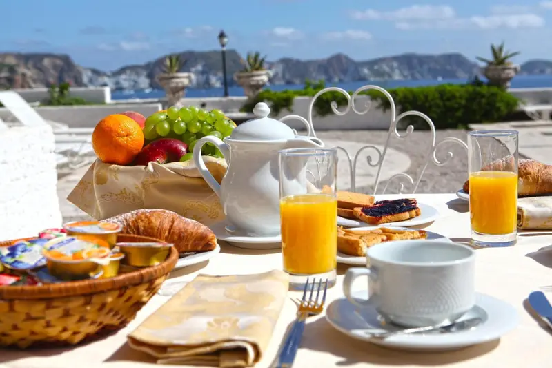 Une table est dressée avec un petit-déjeuner composé de fruits, de viennoiseries et de boissons.