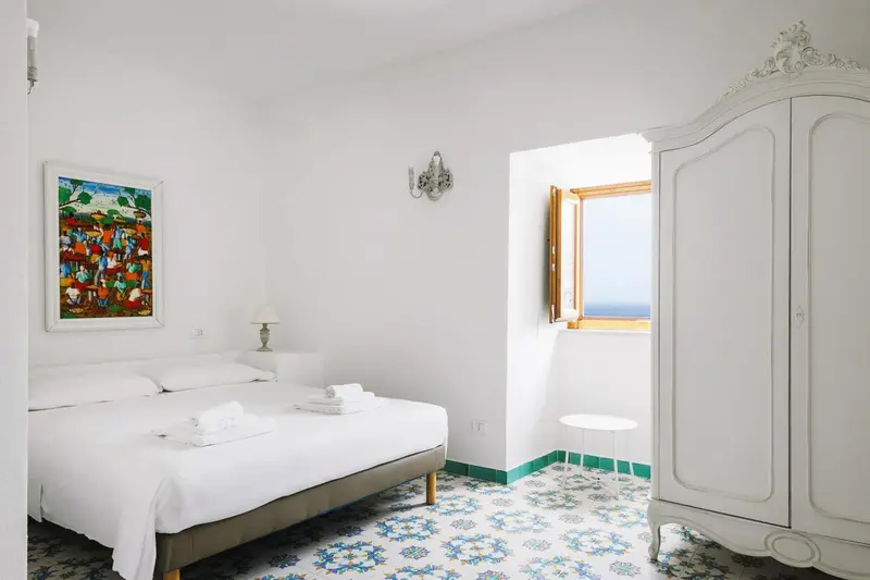Chambre lumineuse avec un lit recouvert de linge blanc et une fenêtre donnant sur la mer.