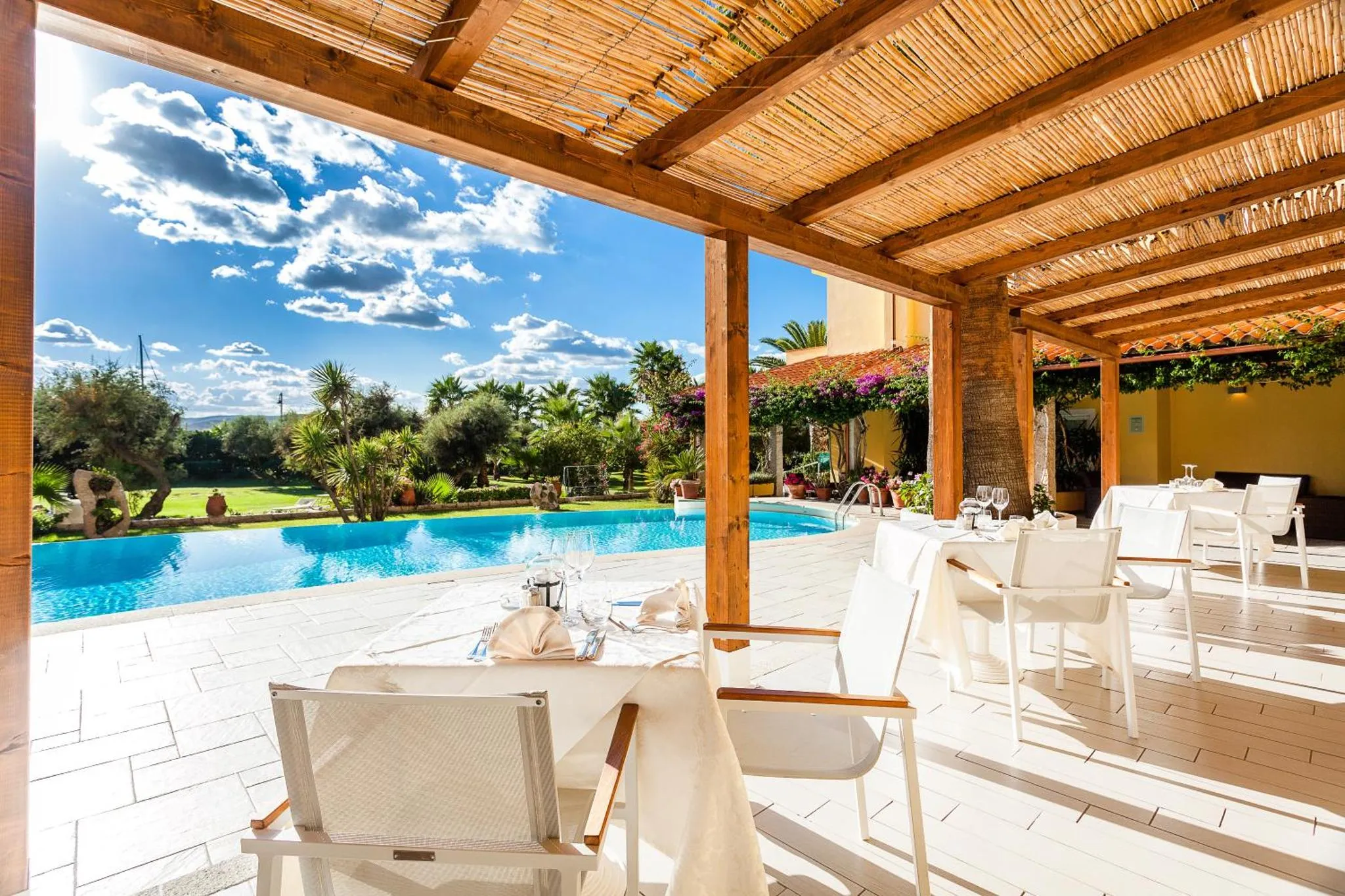 Terrasse ombragée donnant sur une piscine et un jardin luxuriant.
