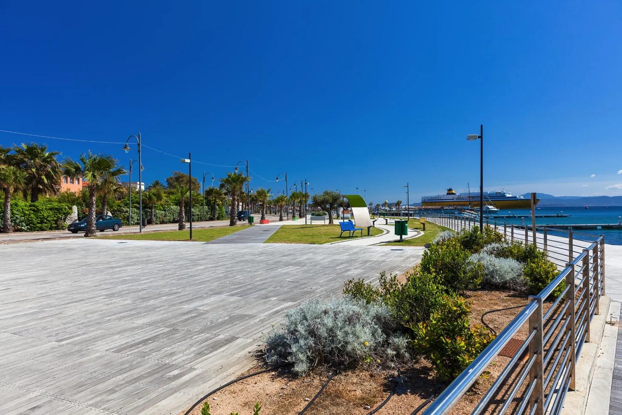Promenade en bord de mer avec des bancs et des palmiers sous un ciel bleu.