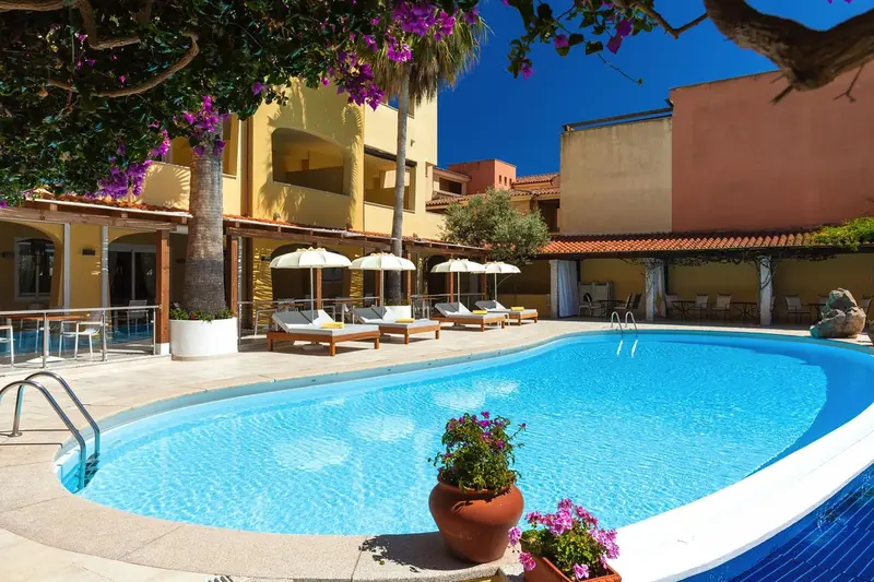 Une piscine rectangulaire bordée de transats et de parasols, devant un bâtiment jaune et orange.