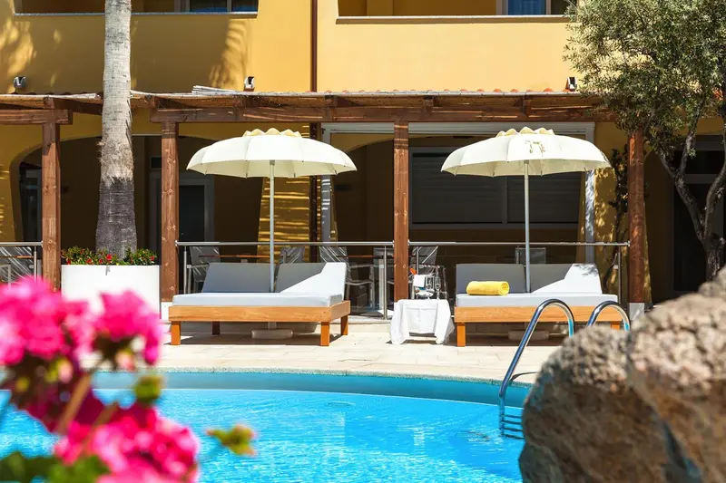 Transats blancs sous des parasols près d'une piscine bleue.