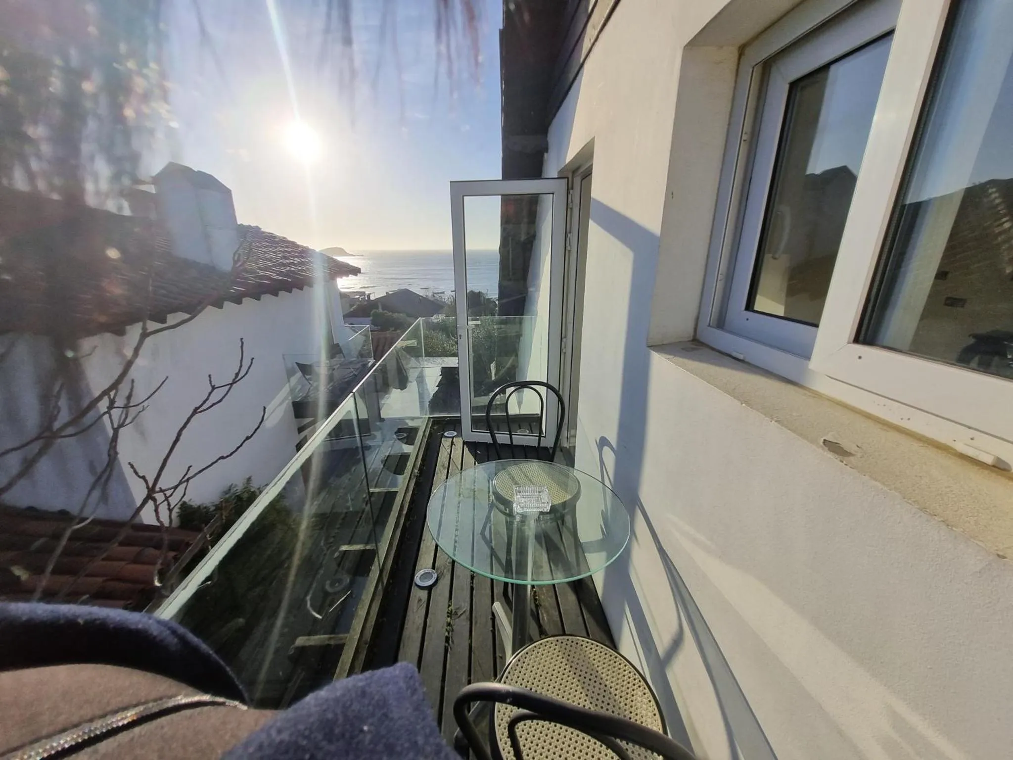 Une terrasse avec une table en verre et des chaises offre une vue sur la mer.