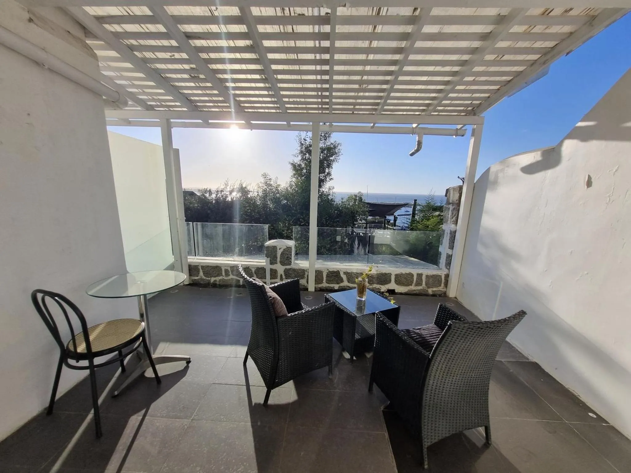 Terrasse ombragée avec mobilier de jardin et vue sur la mer.