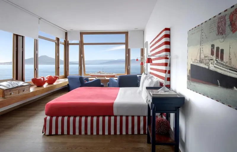 Chambre lumineuse avec un lit rouge et blanc donnant sur une vue mer.