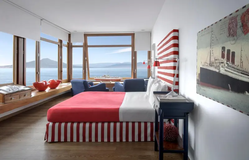 Une chambre lumineuse avec un lit rouge et blanc donnant sur la mer.