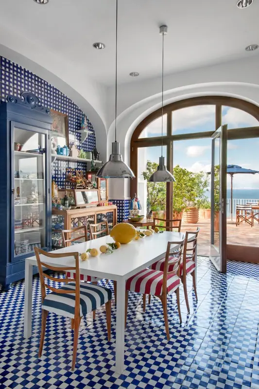 Une salle à manger lumineuse avec une table blanche et des chaises rayées, donnant sur une terrasse ensoleillée.