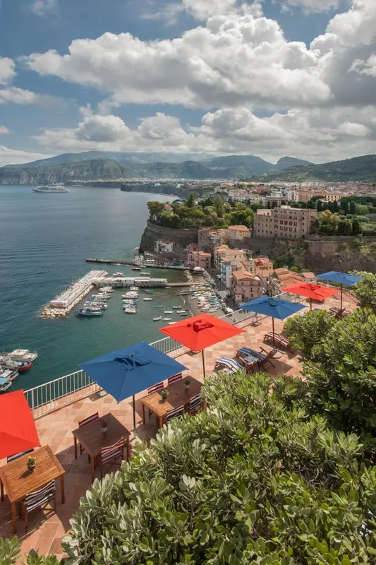 Terrasse avec tables et parasols surplombant une côte rocheuse et une marina.