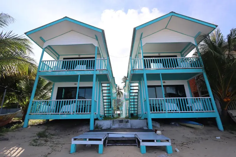 Deux bungalows turquoise avec balcon face à une plage de sable.