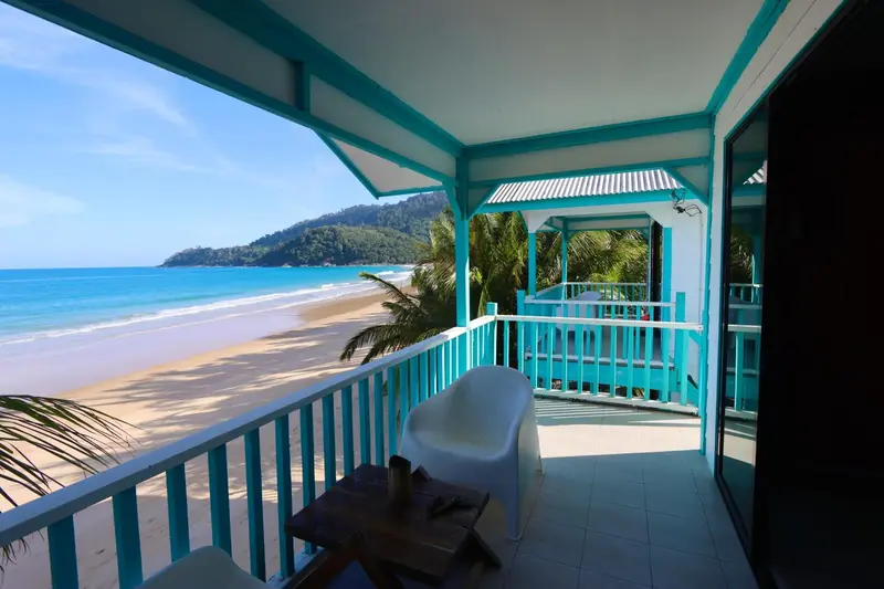 Terrasse avec mobilier blanc donnant sur une plage de sable fin et une mer turquoise.