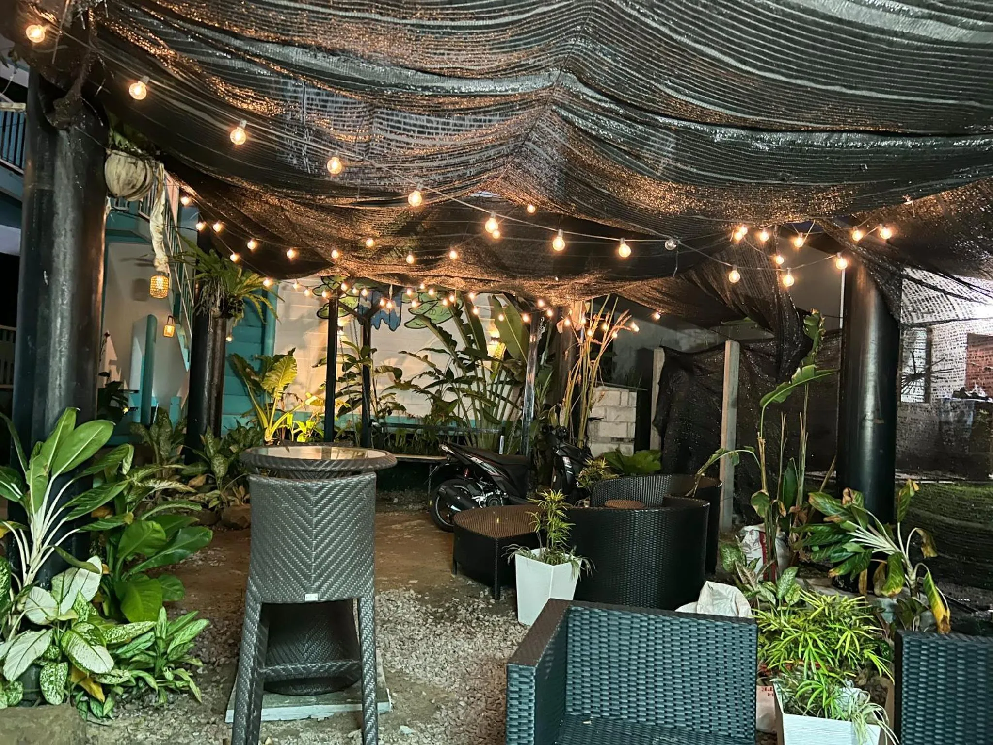 Espace de détente extérieur ombragé avec mobilier en résine tressée et végétation tropicale.