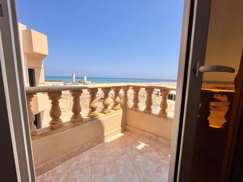 Balcon avec vue sur une plage de sable clair et une mer turquoise.