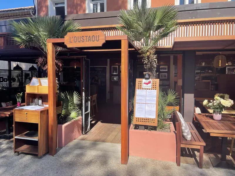 Terrasse ombragée avec tables et chaises devant un restaurant.