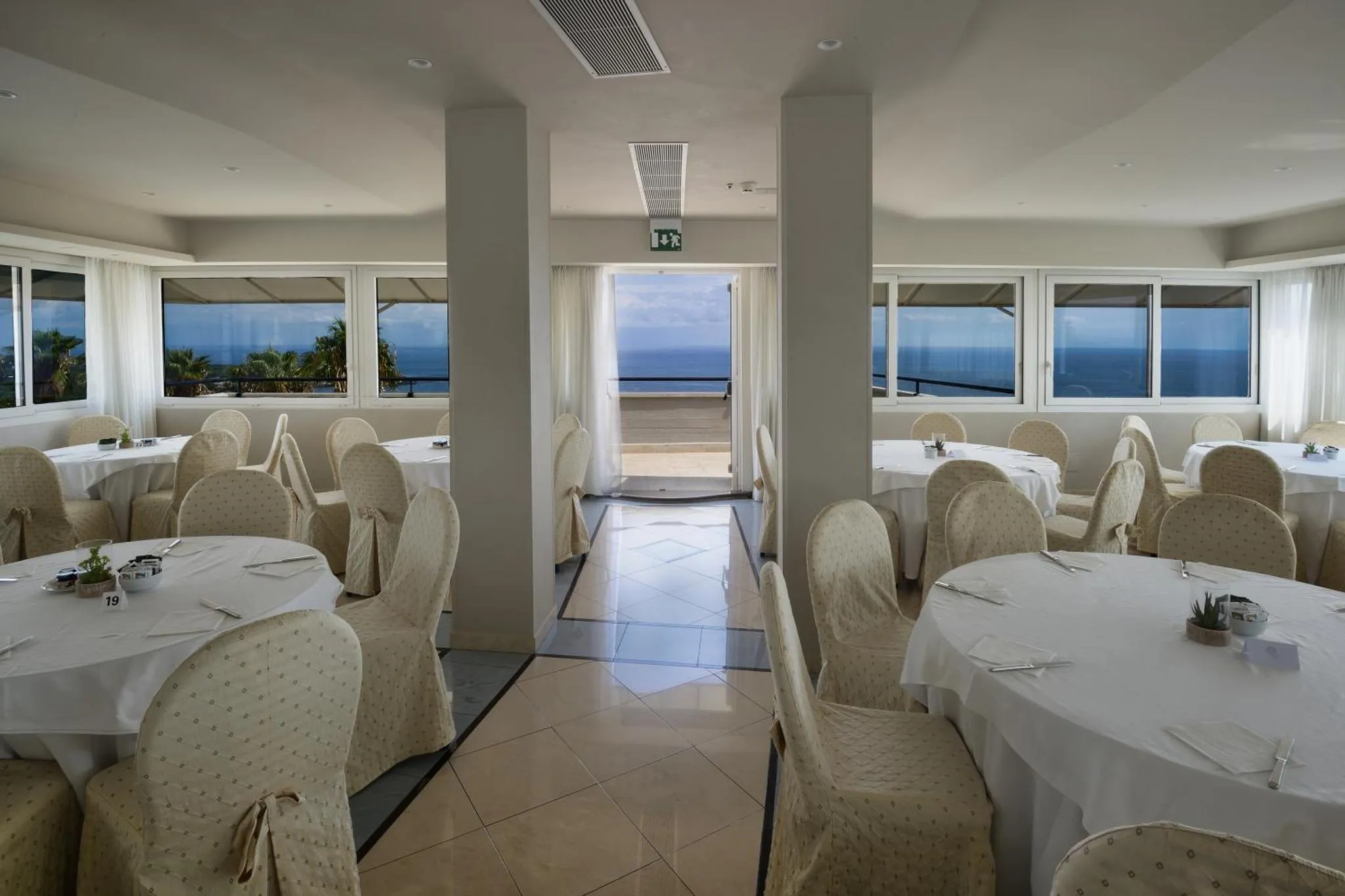 Une salle lumineuse avec des tables dressées pour un repas face à la mer.