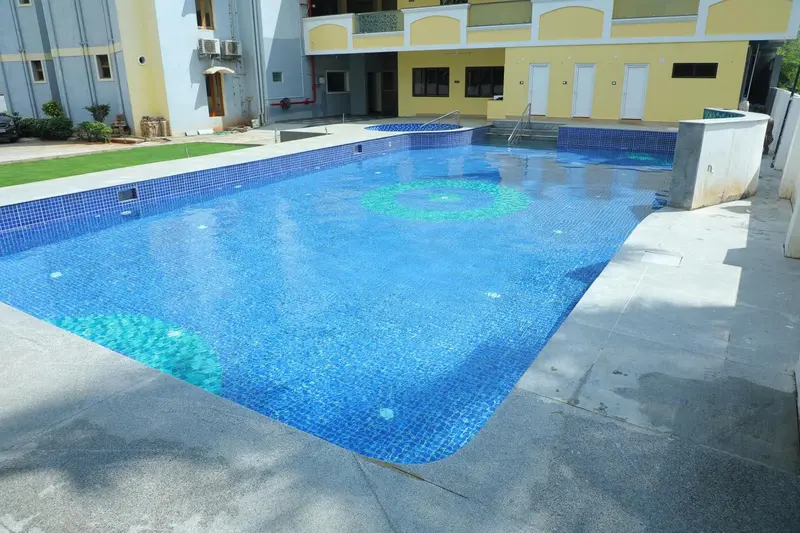 Piscine rectangulaire turquoise entourée d'un dallage gris et d'une pelouse verte.