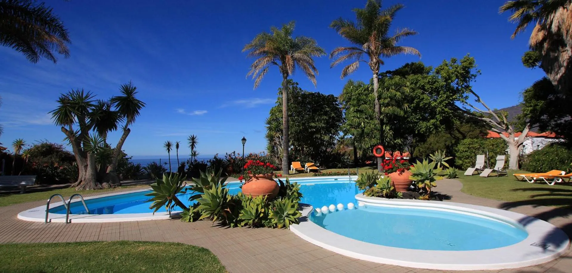Piscine turquoise entourée de végétation luxuriante avec vue sur la mer.
