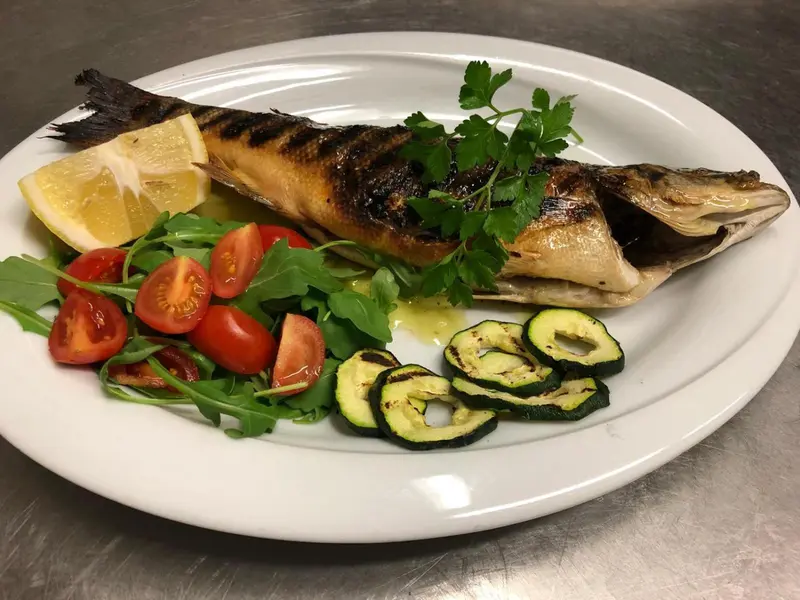 Un poisson grillé est servi avec des légumes et une tranche de citron sur une assiette blanche.