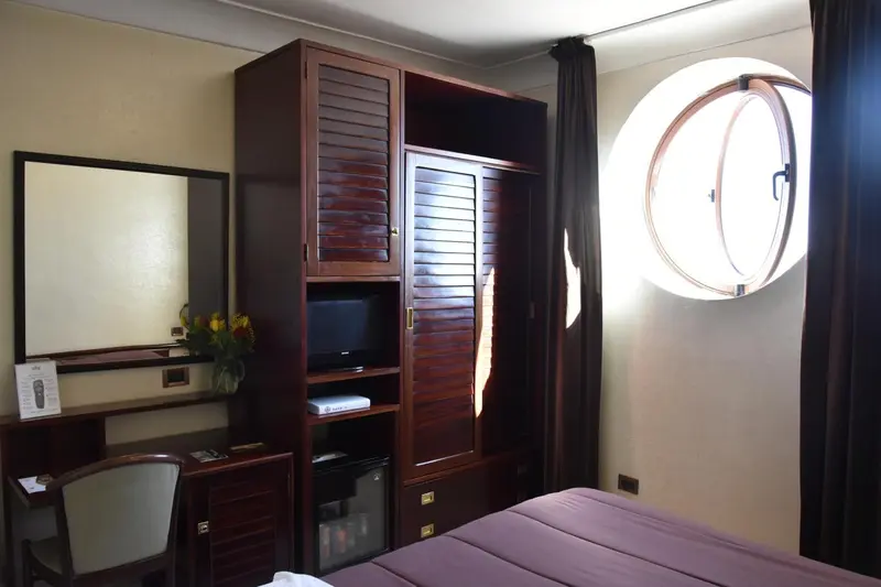 Une chambre lumineuse avec un bureau, un placard et une fenêtre ronde.