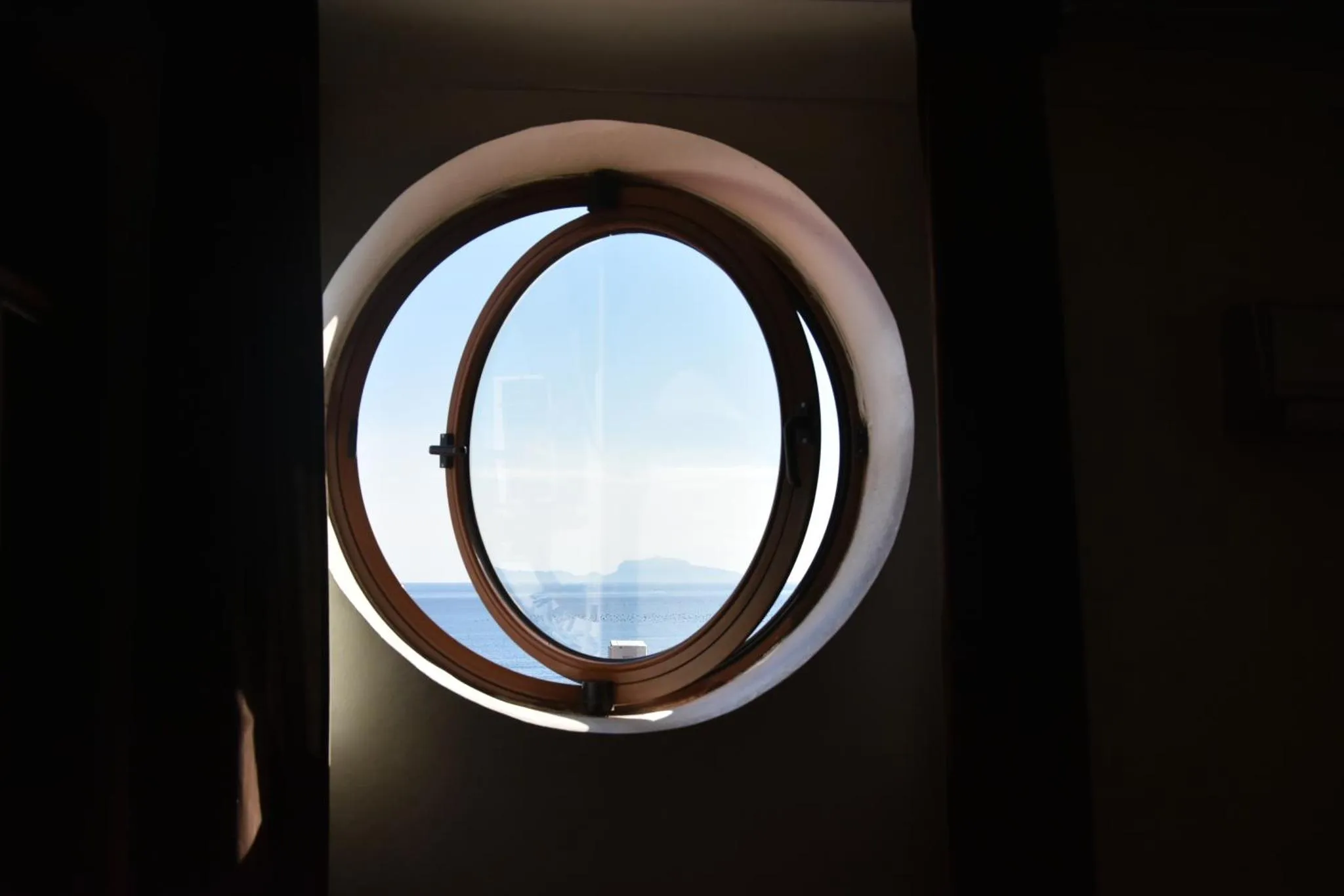 Une vue sur la mer est encadrée par une fenêtre ronde.