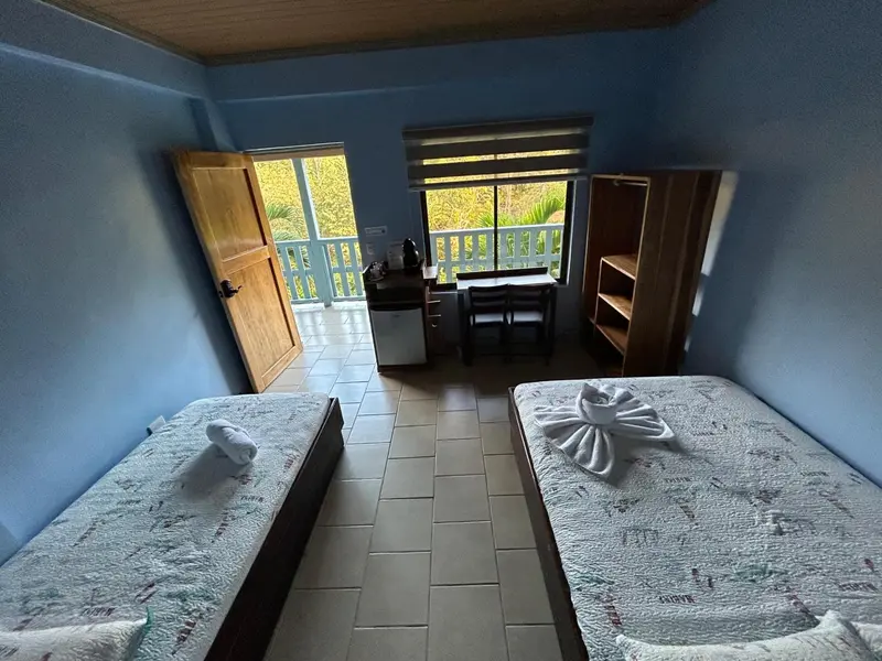 Une chambre lumineuse avec deux lits et un coin repas donnant sur l'extérieur.