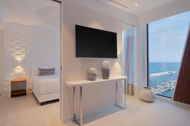Une chambre lumineuse avec un lit et une vue sur la mer et un port de plaisance.