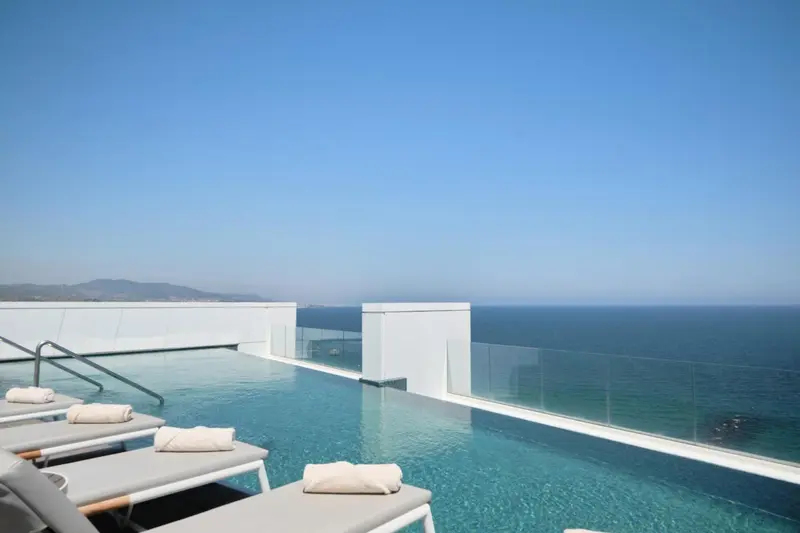 Transats et piscine à débordement avec vue sur la mer et les montagnes.