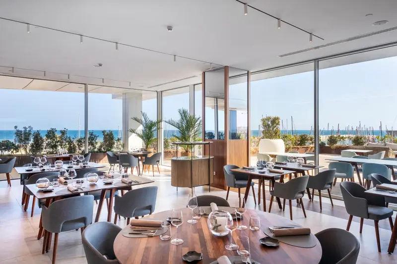Une salle lumineuse avec des tables dressées face à une vue sur la mer.
