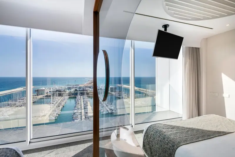 Une chambre lumineuse avec une grande baie vitrée donnant sur un port de plaisance.
