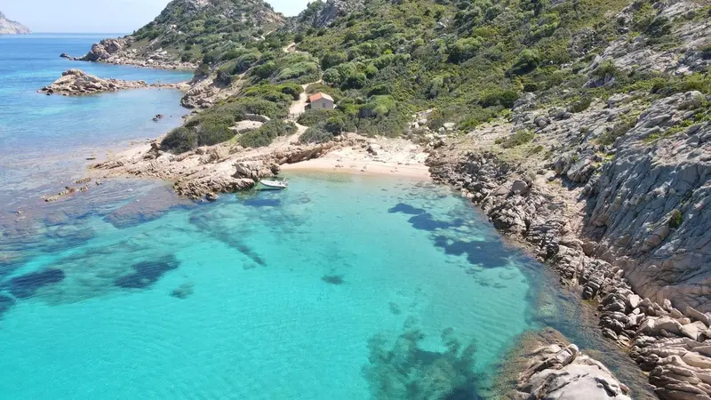 Vue aérienne d'une crique rocheuse avec une plage et une eau turquoise.